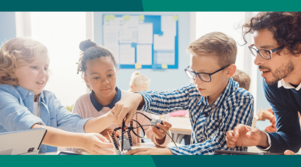 A group of students working together in class with their teacher next to them.