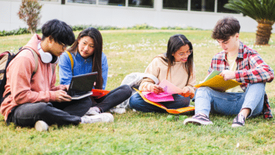 cheerful college students sitting on grass at campus