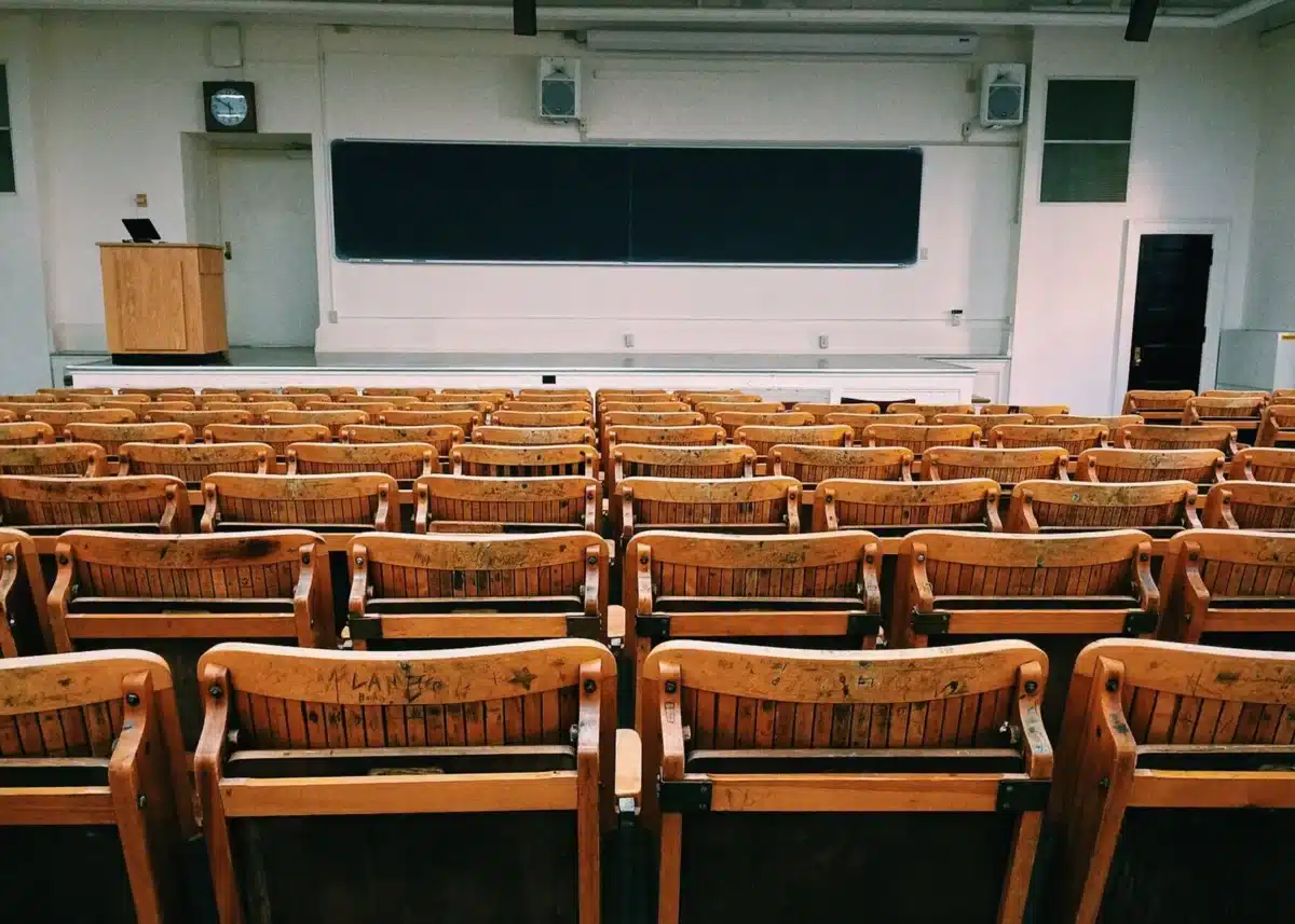 View of an empty classroom. Many rows of wooden chairs.