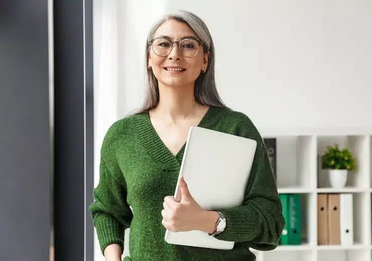 Woman with glasses in a green sweater holding a tablet.