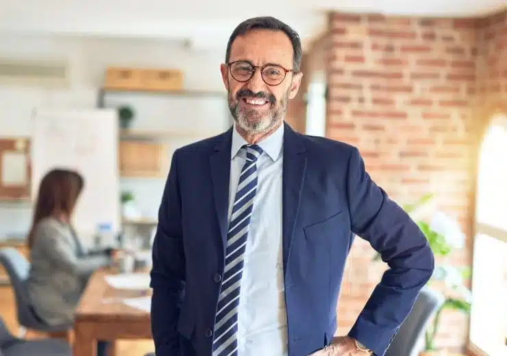 Smiling man in a blue suit and tie posing for a photo in an office.